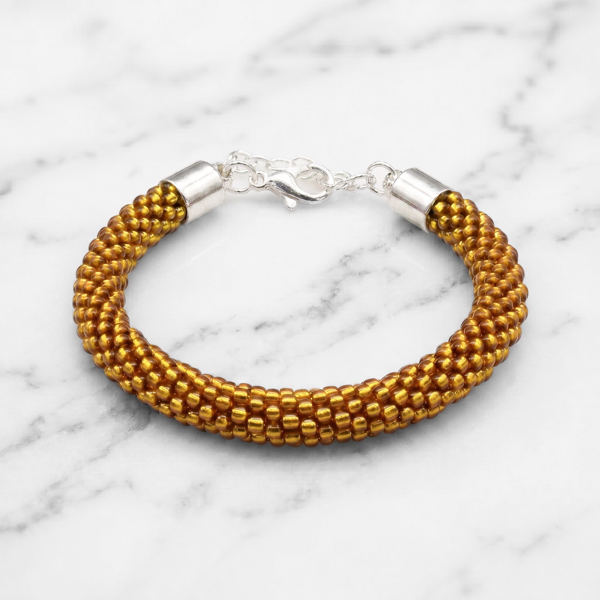 Gold beaded bracelet with silver clasp on a marble background
