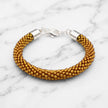 Gold beaded bracelet with silver clasp on a marble background